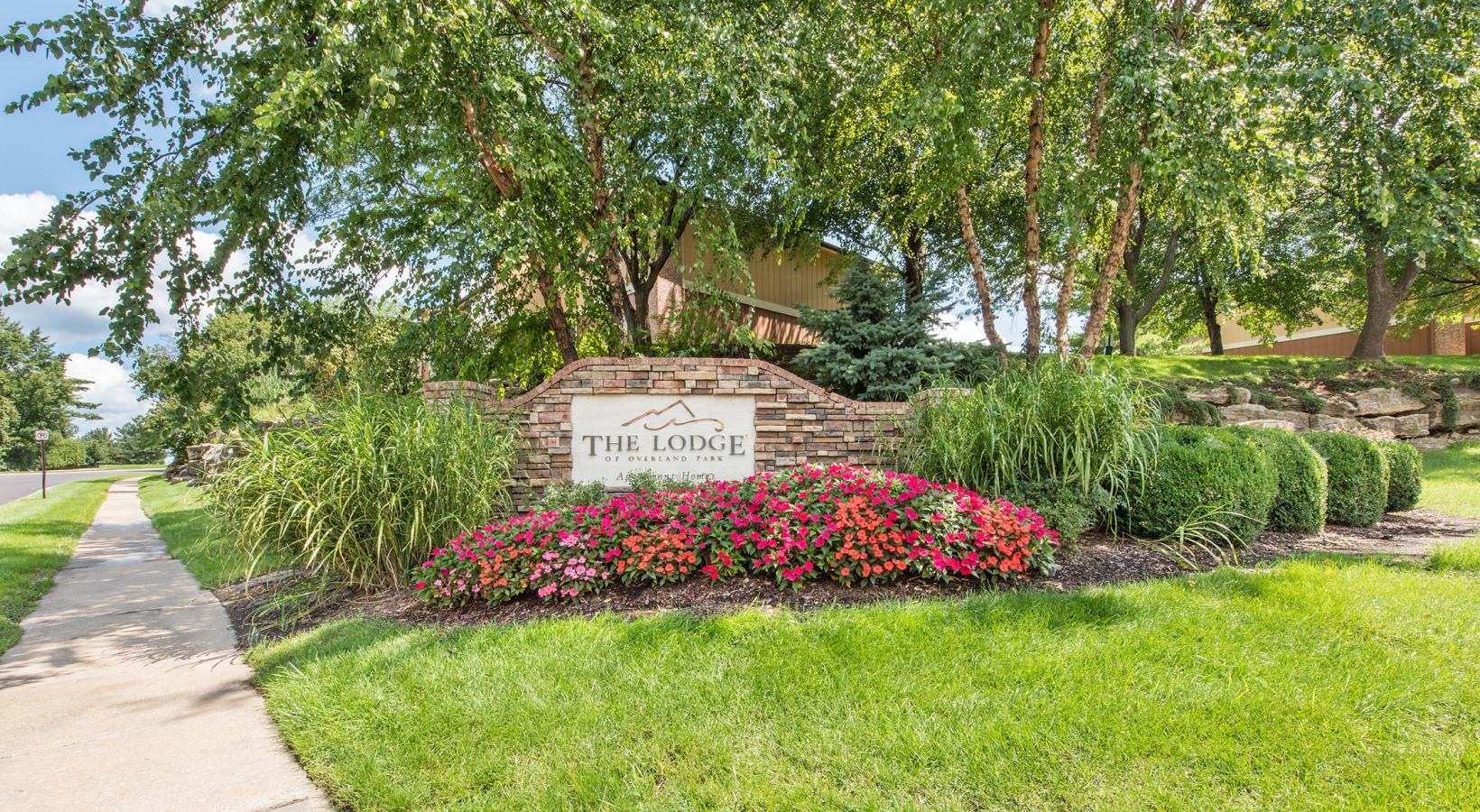 Settle into comfort at The Lodge of Overland Park a sign in a garden that reads the lodge