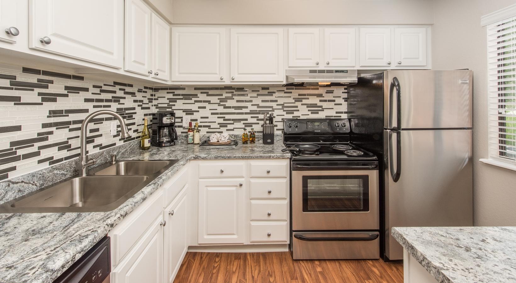 Beautiful kitchens with designer finishes a kitchen with white cabinets a sink a fridge a stovetop